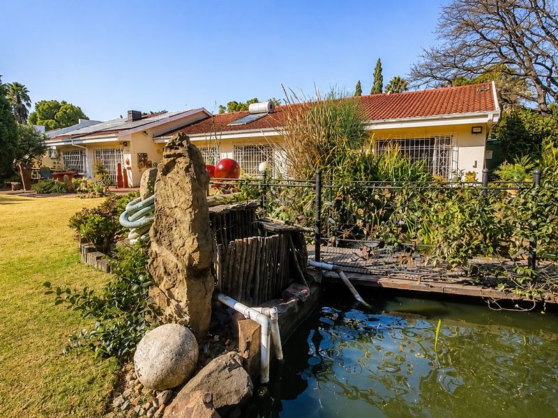 Rear view of the property featuring a landscaped garden, a pond with a small bridge, and a tiled roof house with security bars.