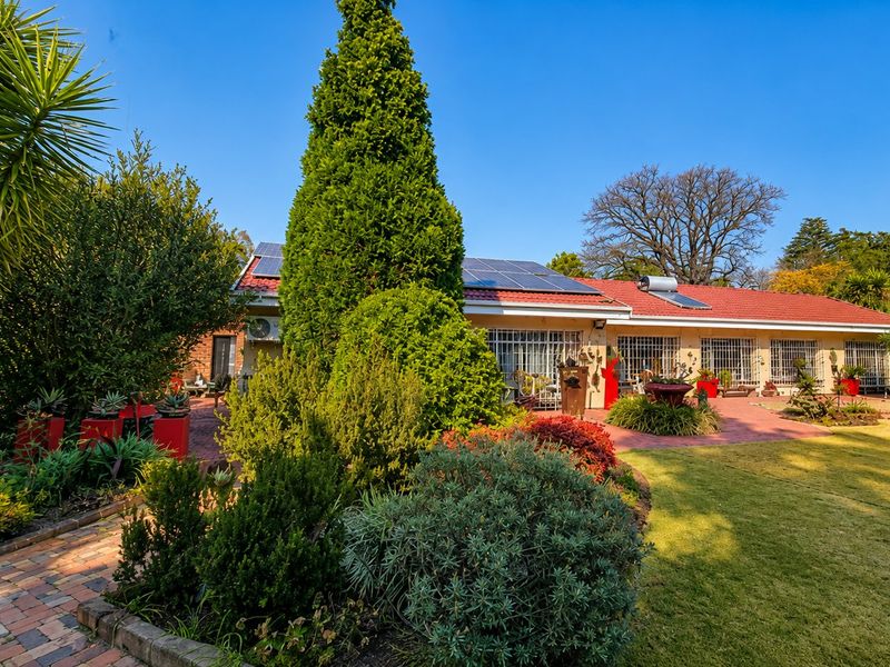 Rear view of the house featuring a spacious brick-paved patio, landscaped garden, solar panels, and a solar water heating system.