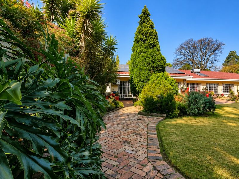 A well-maintained rear garden featuring a brick paved pathway leading to the house, surrounded by lush landscaping and mature trees.