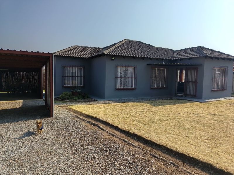Front elevation of a single-story house featuring a tiled roof, security bars on windows, and an attached carport with a gravel driveway.