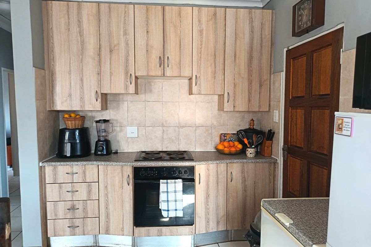 A functional kitchen featuring wood-look laminate cabinetry, built-in oven, electric hob, and tiled backsplash with neutral floor tiles.