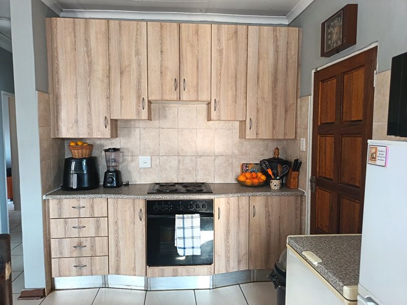 A functional kitchen featuring wood-look laminate cabinetry, built-in oven, electric hob, and tiled backsplash with neutral floor tiles.