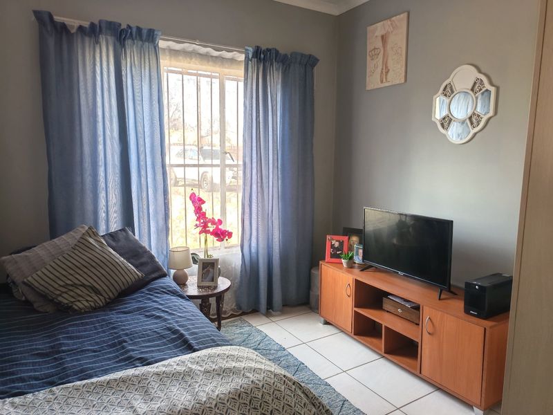 A bedroom featuring tiled flooring and a window fitted with security bars, providing a functional and well-lit living space.
