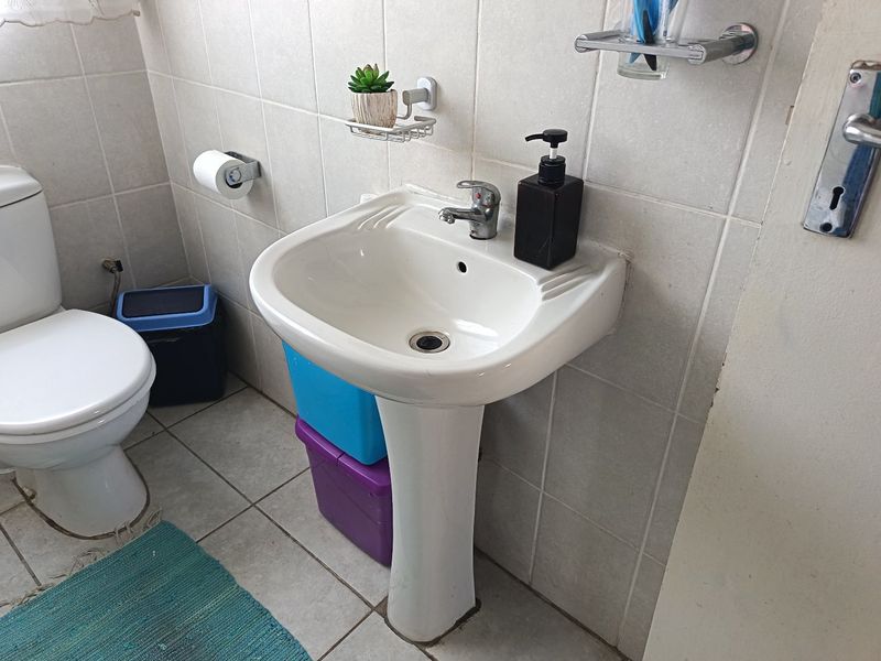 A functional bathroom featuring a white pedestal basin, ceramic wall and floor tiling, and a standard toilet.