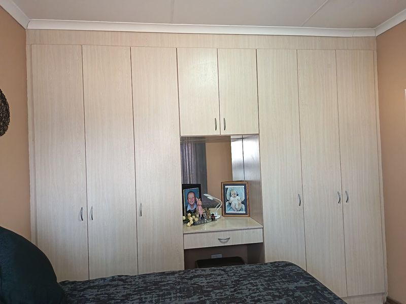 A bedroom featuring extensive light wood-grain built-in cupboards with an integrated central vanity and mirror.