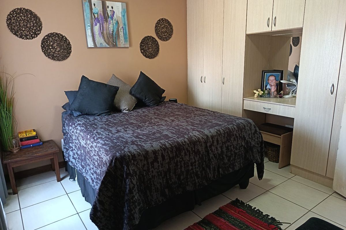 A bedroom featuring light wood-toned built-in cupboards with an integrated vanity unit and neutral tiled flooring.