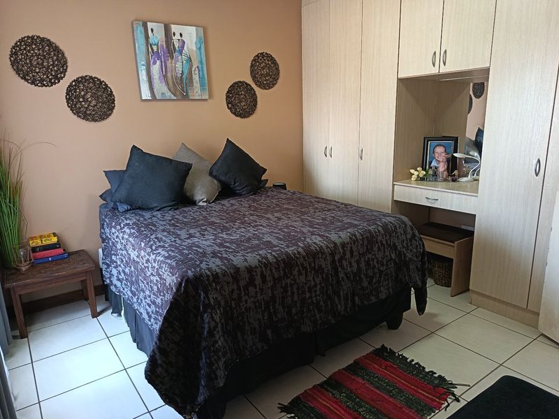 A bedroom featuring light wood-toned built-in cupboards with an integrated vanity unit and neutral tiled flooring.