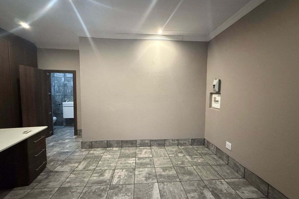 An open-plan living area featuring neutral wall tones, tiled flooring, built-in cabinetry, and recessed lighting, with an adjacent bathroom visible.