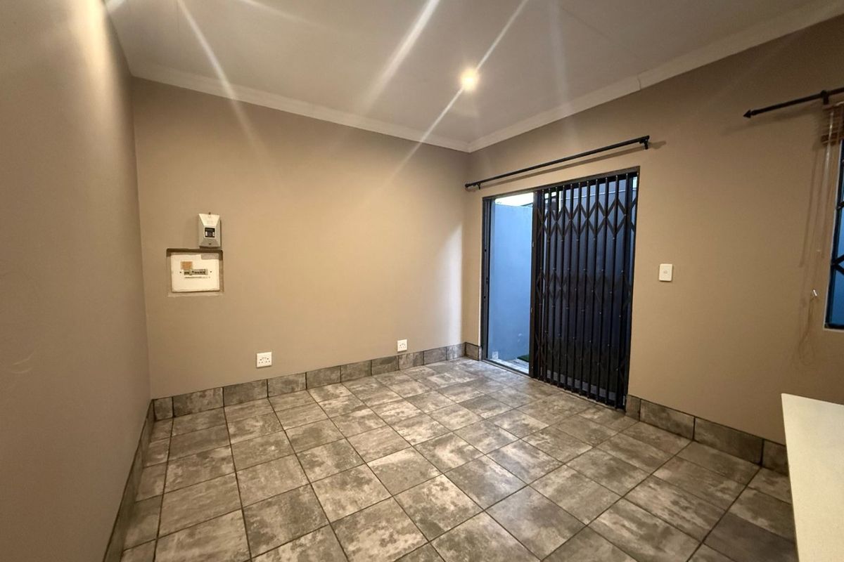 An empty living area featuring neutral wall tones, durable tiled flooring, and a secure sliding door leading to an outdoor space.
