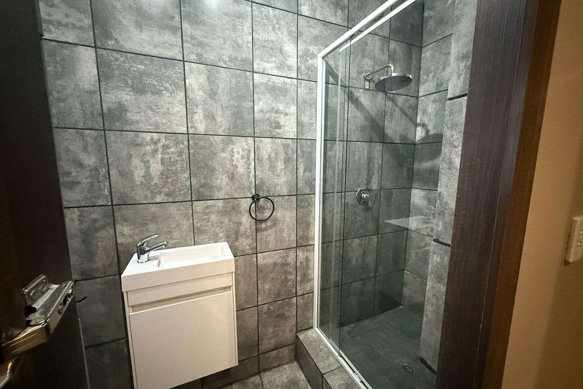 A modern bathroom featuring grey textured wall tiles, a glass-enclosed shower, and a compact wall-mounted vanity with a basin.