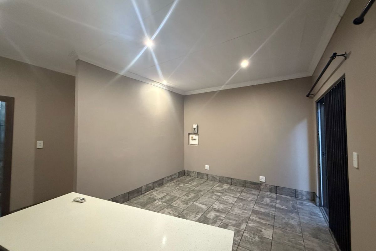 An open-plan living area featuring neutral walls, tiled flooring, recessed lighting, and a sliding door providing access to the exterior.