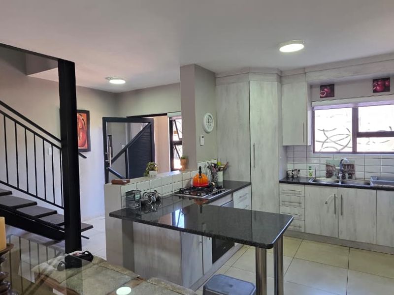 Open-plan kitchen and dining area featuring modern cabinetry, granite countertops, gas hob, and a staircase with a metal balustrade.