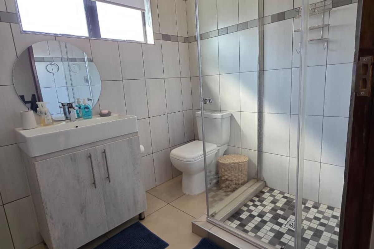A functional bathroom featuring a vanity cabinet, toilet, and a glass-enclosed shower with decorative tiled flooring.