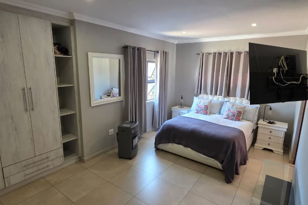 A well-maintained bedroom featuring neutral tiled flooring, recessed lighting, and a large built-in wardrobe with integrated shelving.