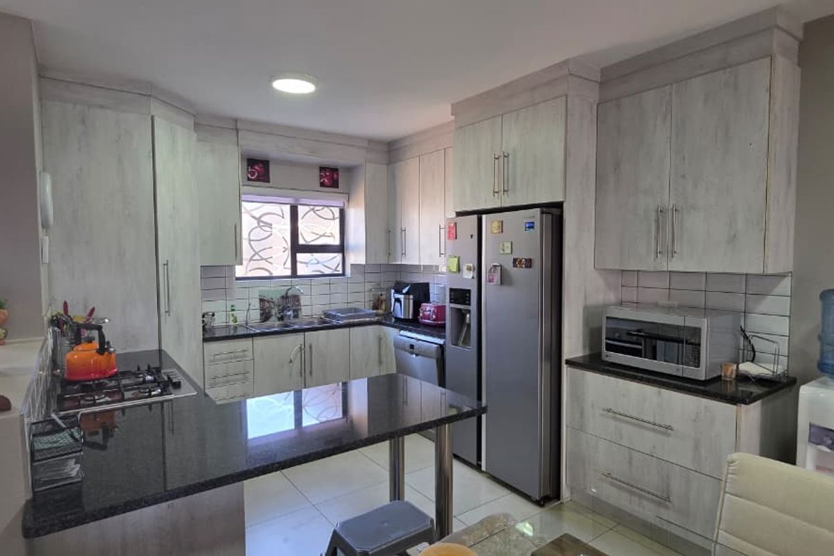 A functional kitchen featuring light-toned built-in cabinetry, granite countertops, a gas hob, and tiled flooring, offering a practical layout for daily meal preparation.