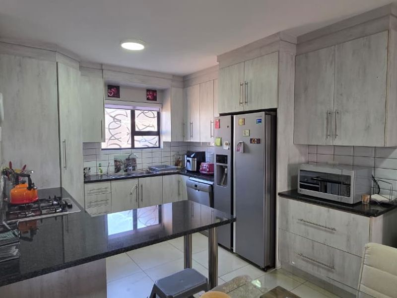 A functional kitchen featuring light-toned built-in cabinetry, granite countertops, a gas hob, and tiled flooring, offering a practical layout for daily meal preparation.