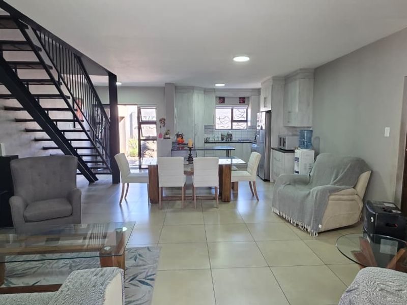 Spacious open-plan living and dining area featuring a modern metal staircase, neutral tiled flooring, and an integrated kitchen with ample cabinetry.
