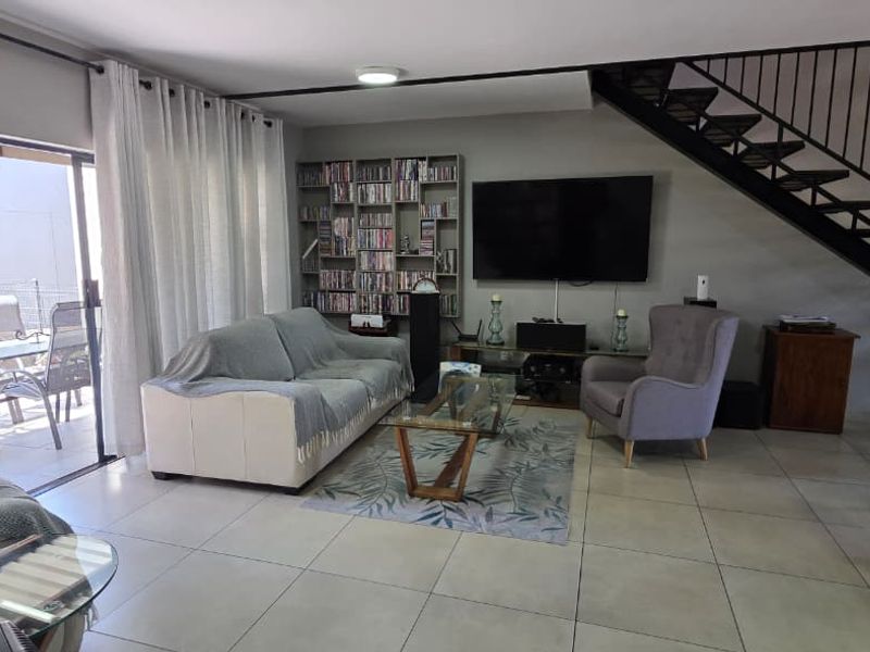 Open plan living area featuring tiled floors, a built-in shelving unit, and a metal staircase leading to the upper level with access to a patio.