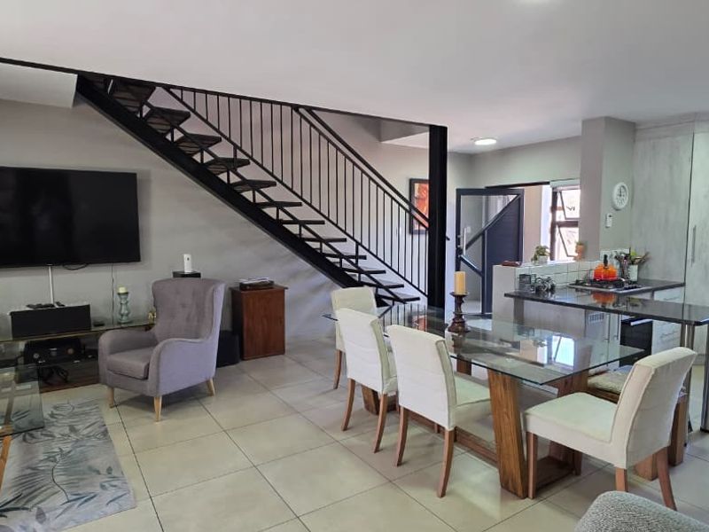 Spacious open-plan living and dining area featuring a modern kitchen with island, tiled floors, and a striking metal staircase leading to the upper level.