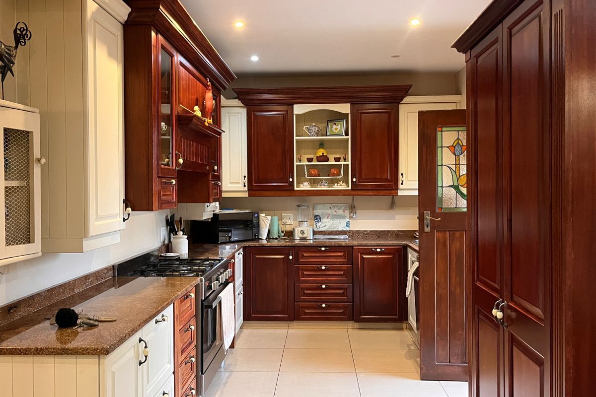 A well-maintained kitchen featuring a mix of dark wood and cream cabinetry, granite countertops, gas hob, and a distinctive stained glass door.