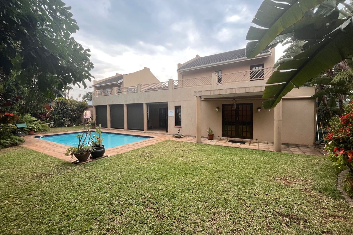 Rear view of the property featuring a swimming pool, a paved patio area, a lawn, and an upper-level balcony with railings.
