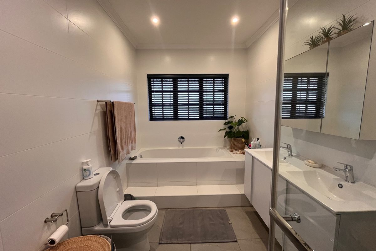Modern bathroom featuring a built-in bathtub, dual vanity with storage, and clean tiled finishes, offering a bright and functional space.