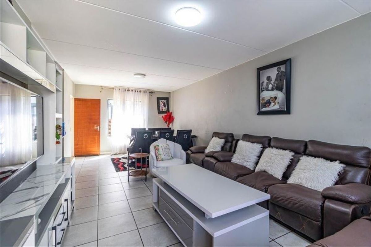 An open-plan living and dining area featuring tiled flooring, neutral wall finishes, and a built-in shelving unit.