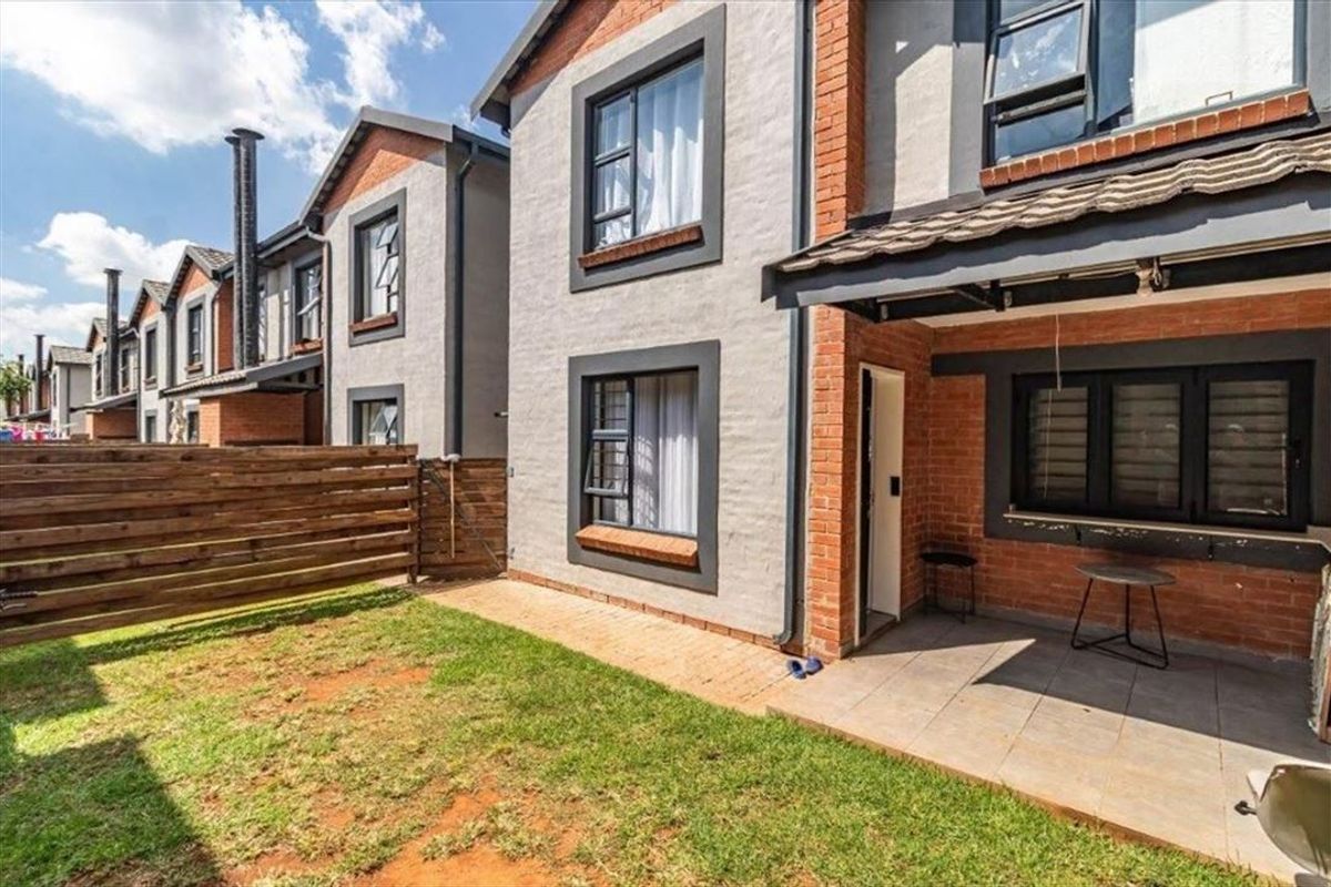 Rear view of the apartment featuring a paved patio area, small private garden with timber fencing, and modern brick and plaster facade.