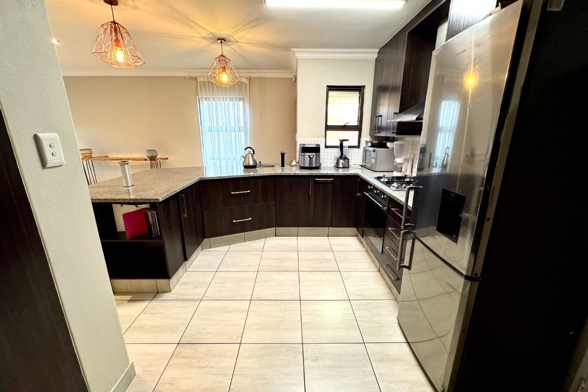 A functional kitchen featuring dark wood cabinetry, granite countertops, a gas hob, and tiled flooring, offering a practical layout for daily cooking.