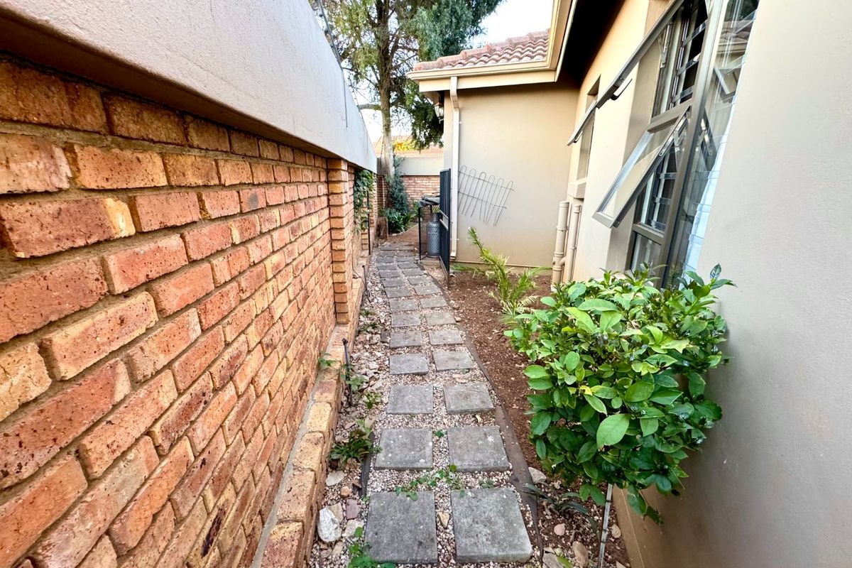 A side passage of the property featuring a brick boundary wall, a paved walkway, and access to the rear garden area.