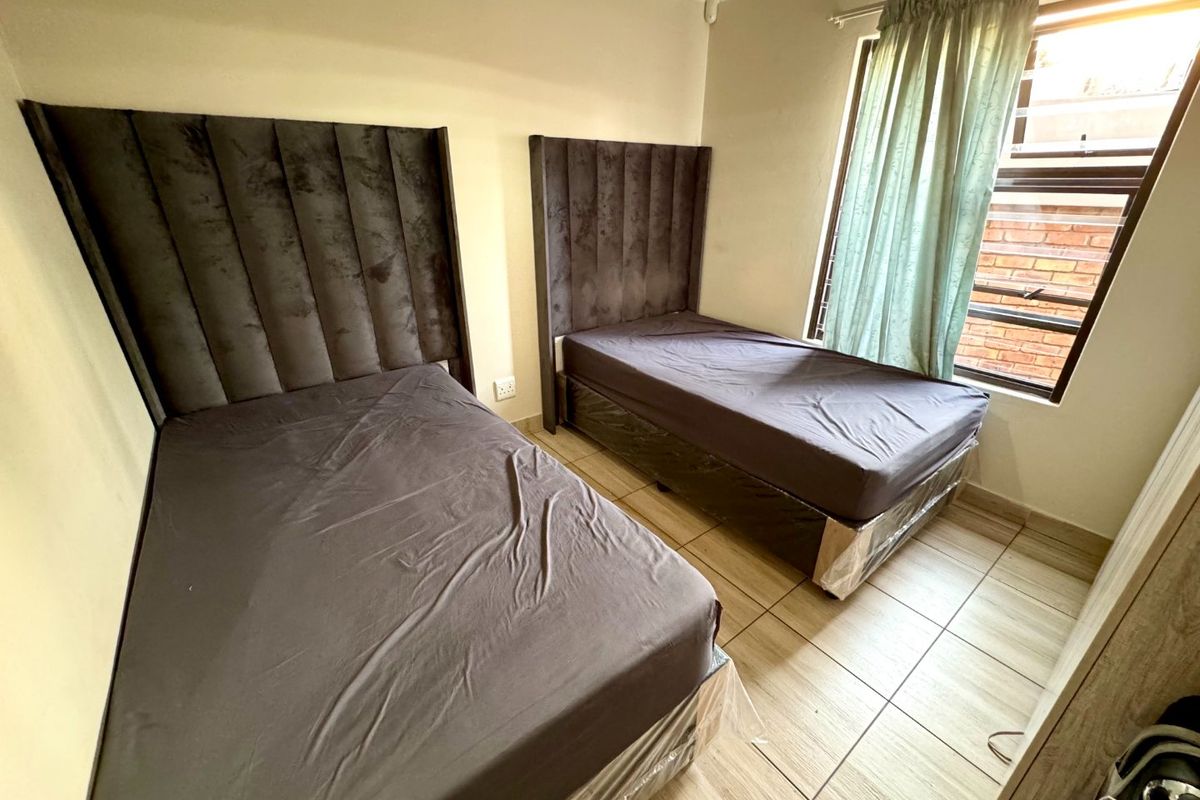 A functional bedroom featuring tiled flooring, neutral walls, and a window with security bars, providing a clean and simple living space.