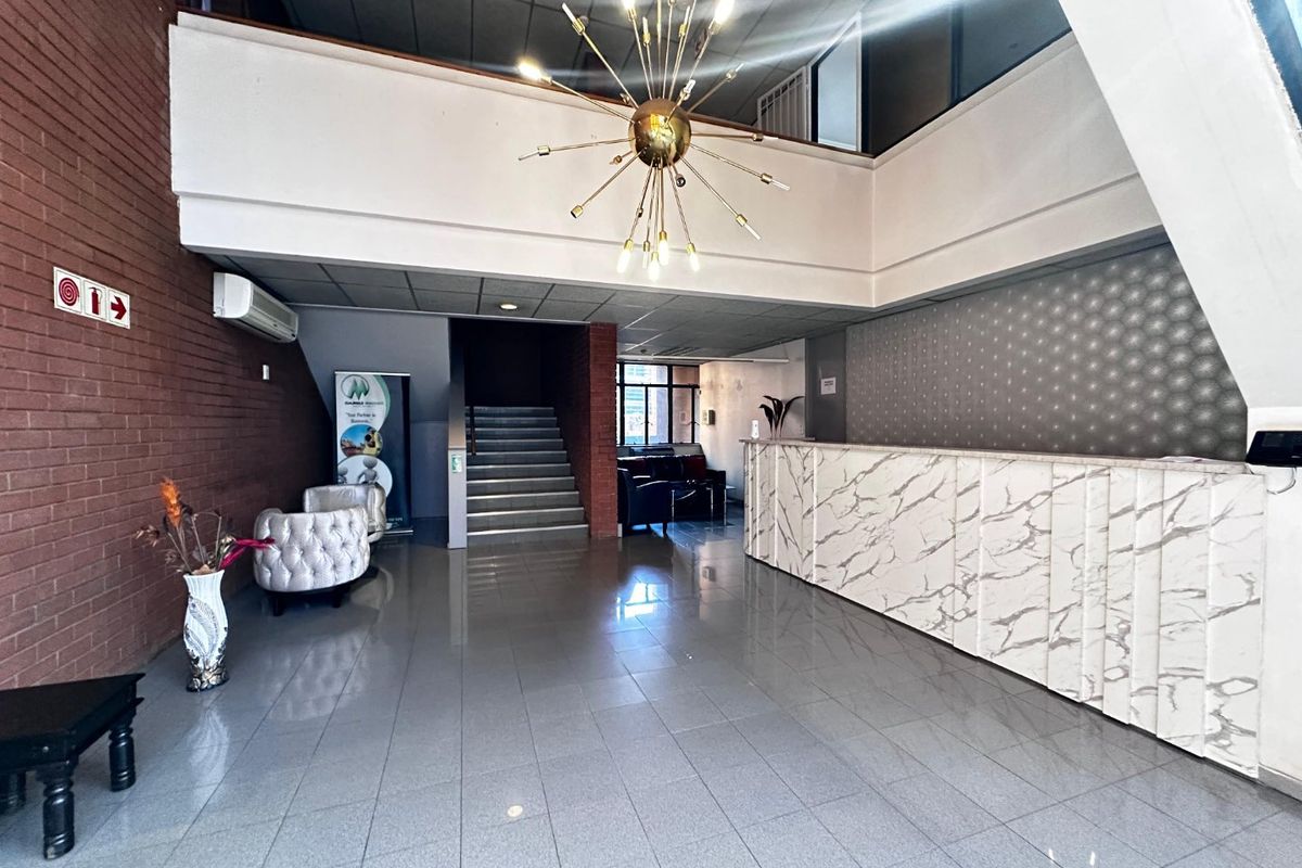 Spacious commercial reception area featuring a marble-look front desk, tiled flooring, exposed brick accents, and a prominent feature light fixture.
