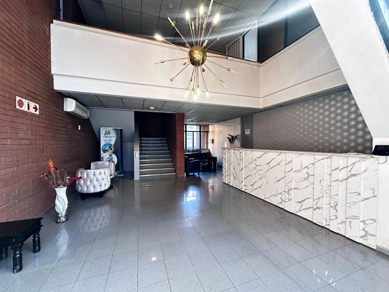 Spacious commercial reception area featuring a marble-look front desk, tiled flooring, exposed brick accents, and a prominent feature light fixture.