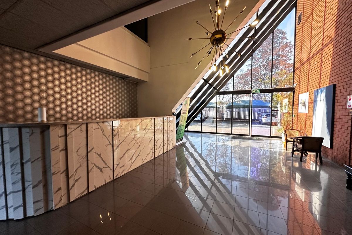 Modern commercial entrance lobby featuring a marble-finish reception desk, polished tile flooring, exposed brickwork, and expansive floor-to-ceiling windows providing natural light.