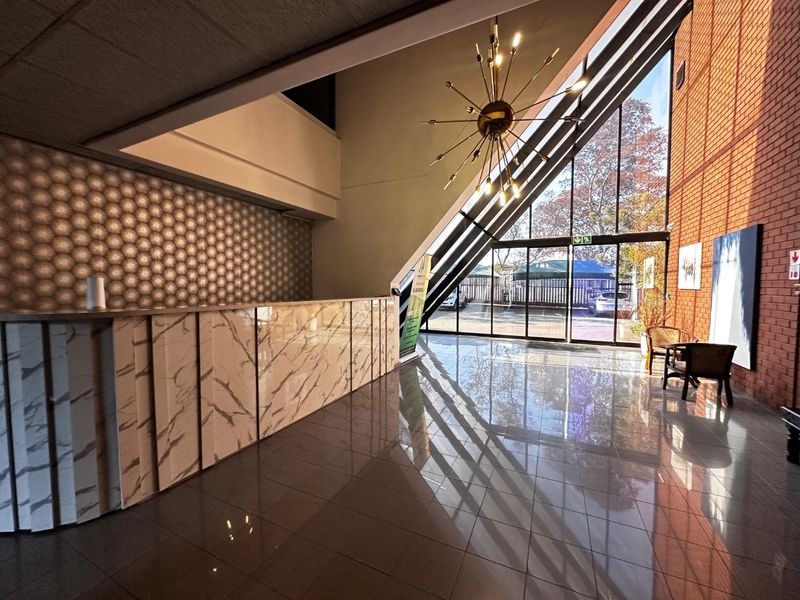 Modern commercial entrance lobby featuring a marble-finish reception desk, polished tile flooring, exposed brickwork, and expansive floor-to-ceiling windows providing natural light.