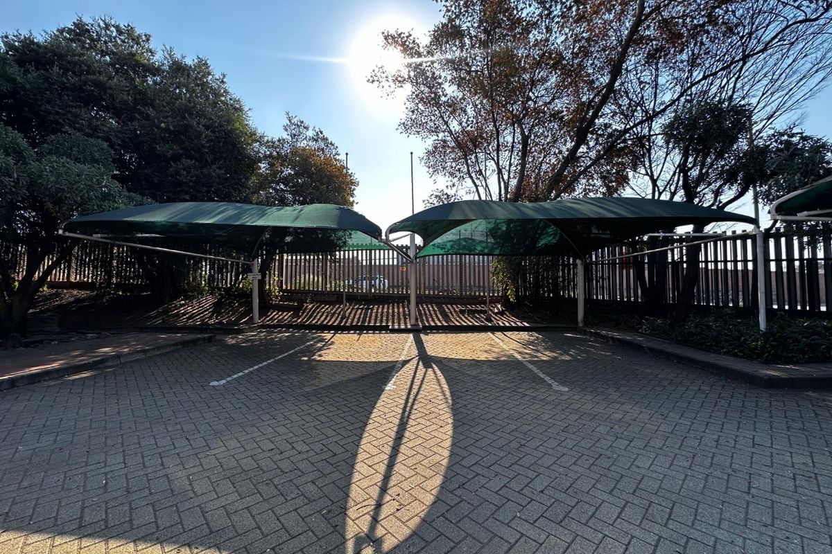 Outdoor parking area featuring paved surfacing and installed shade cloth carports, secured by perimeter fencing.
