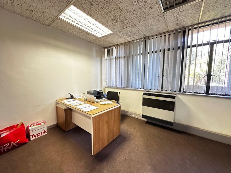 A functional commercial office space featuring a suspended ceiling, recessed lighting, vertical blinds, and a wall-mounted air conditioning unit.