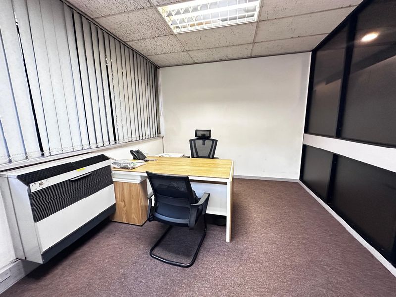 A functional commercial office space featuring a suspended ceiling, vertical blinds, and carpet flooring, suitable for a professional work environment.
