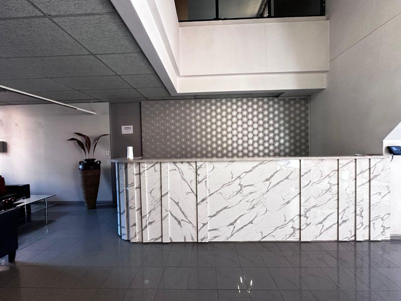 A professional commercial reception area featuring a marble-look desk, textured feature wall, and clean tiled flooring in a modern office setting.