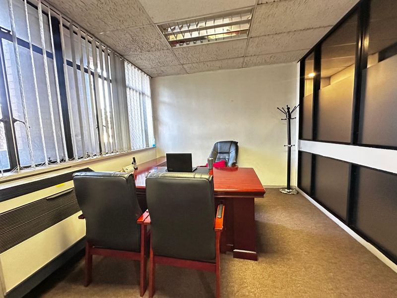 A functional office space featuring a suspended ceiling, recessed lighting, carpeted flooring, and a partitioned glass wall for privacy.