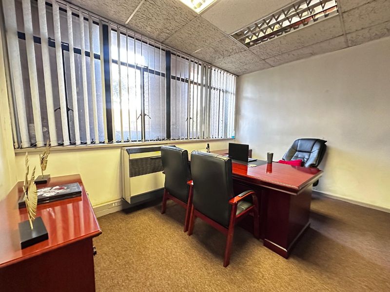 A functional commercial office space featuring a suspended ceiling, recessed lighting, vertical blinds, and a wall-mounted HVAC unit.