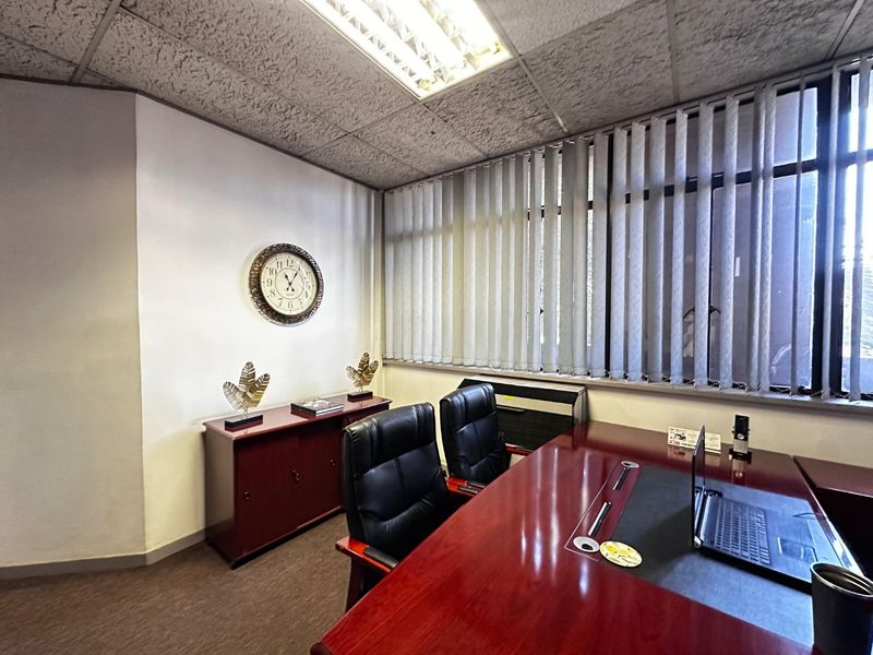 A functional commercial office space featuring a suspended ceiling, vertical blinds, and carpeted flooring, suitable for professional use.