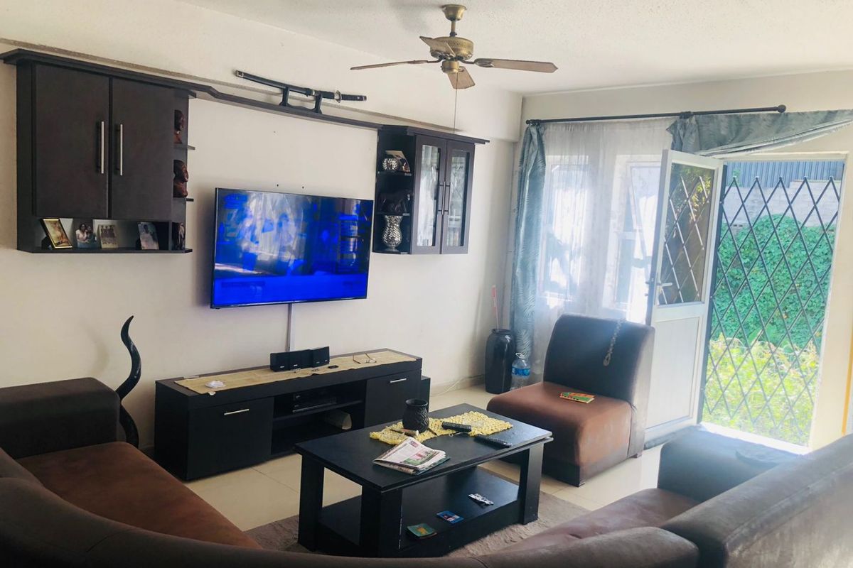 A living room featuring tiled flooring, a ceiling fan, and built-in wall cabinetry, with direct access to an outdoor area through a security gate.