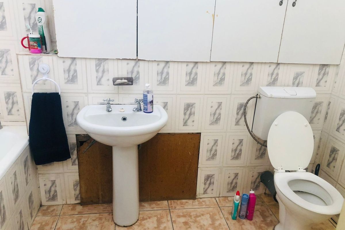 A dated bathroom featuring a pedestal basin, toilet, and wall-mounted cabinetry, requiring cosmetic updates and repairs to the wall tiling and finishes.
