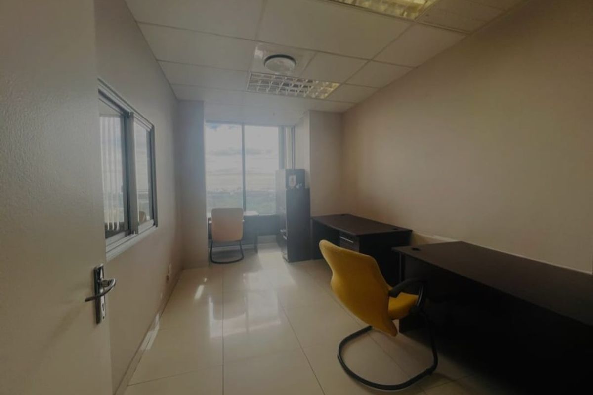 A functional office space featuring tiled flooring, a suspended ceiling with recessed lighting, and a large window providing natural light.