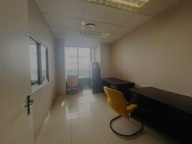 A functional office space featuring tiled flooring, a suspended ceiling with recessed lighting, and a large window providing natural light.
