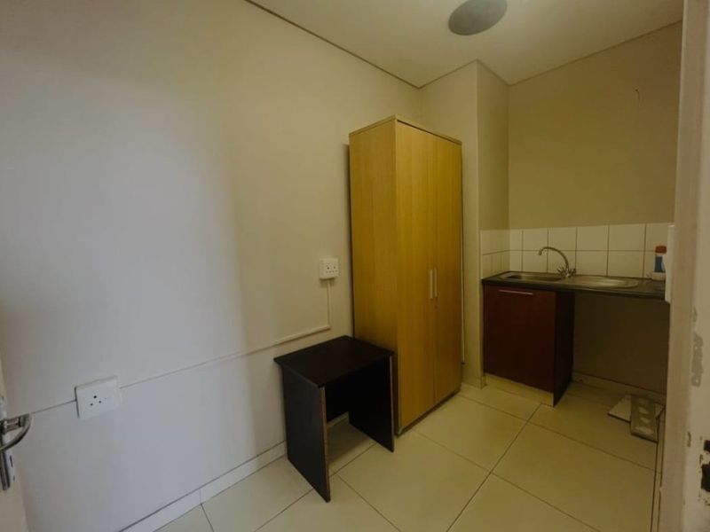 A functional scullery or utility area featuring a stainless steel sink, tiled backsplash, and base cabinetry with tiled flooring.