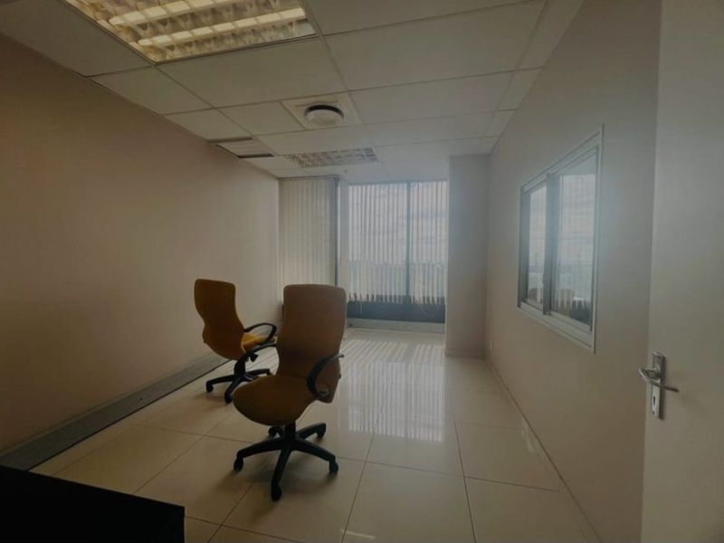 A functional office space featuring tiled flooring, a suspended ceiling with recessed lighting, and large windows with vertical blinds for natural light.