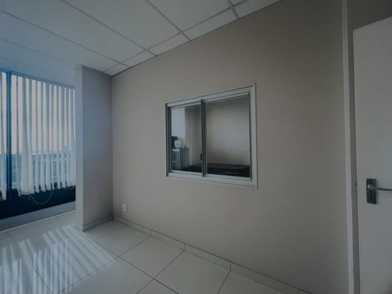 A clean, empty commercial office space featuring tiled flooring, a suspended ceiling, and an internal sliding window for natural light flow.