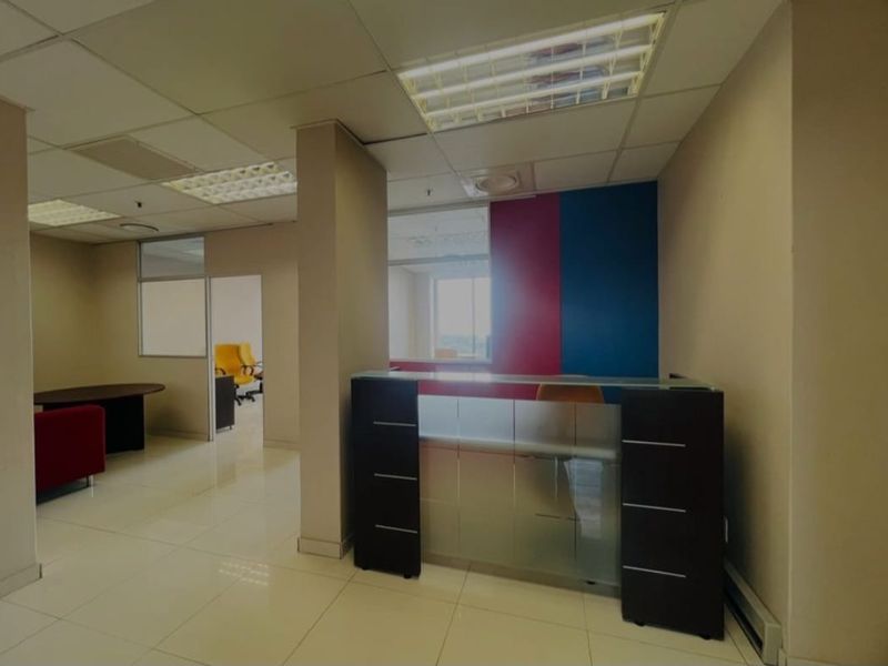 A commercial office space featuring a built-in reception desk, tiled flooring, suspended ceilings with recessed lighting, and glass partition walls for a professional layout.